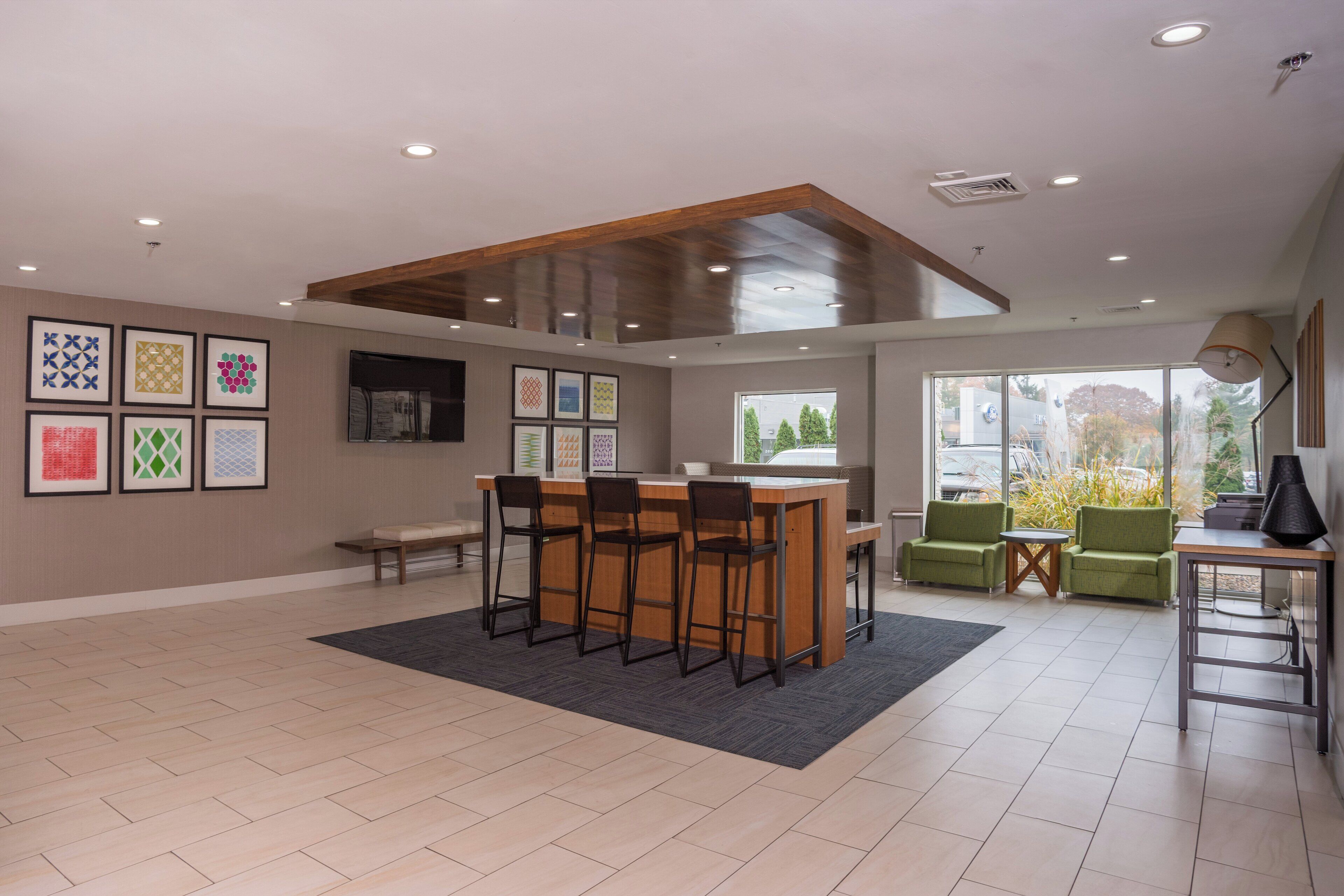 A spacious room with a wooden ceiling, a bar area with stools, green chairs, and framed artwork on the walls.