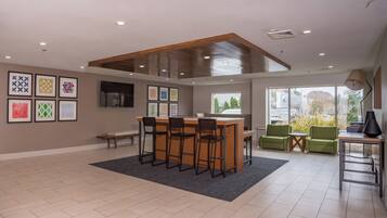 A spacious room with a wooden ceiling, a bar area with stools, green chairs, and framed artwork on the walls.