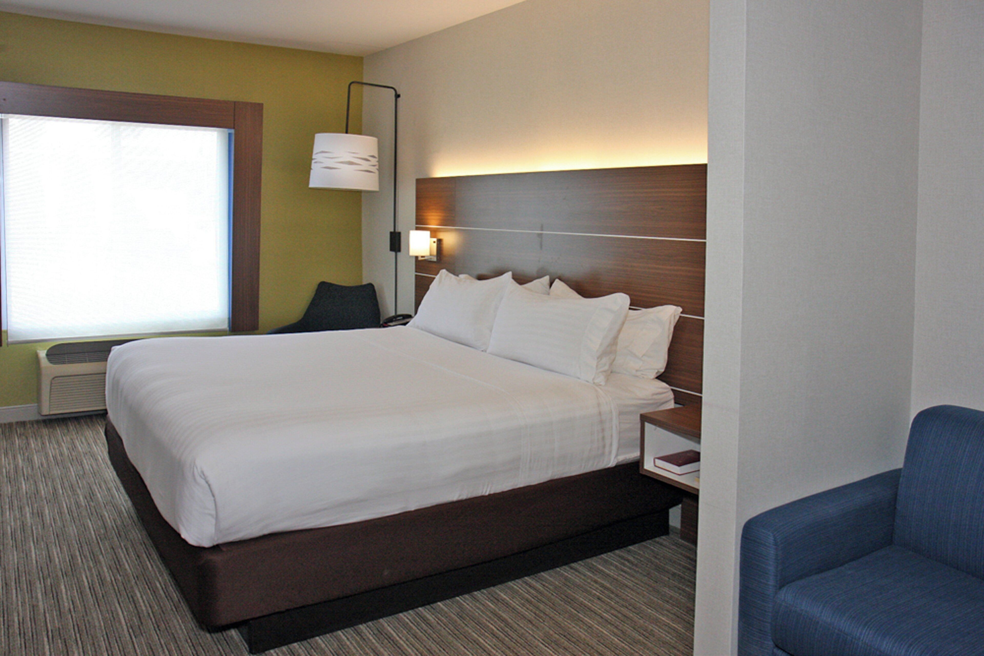 A hotel room with a large bed, a bedside table, a lamp, a chair, and a window.