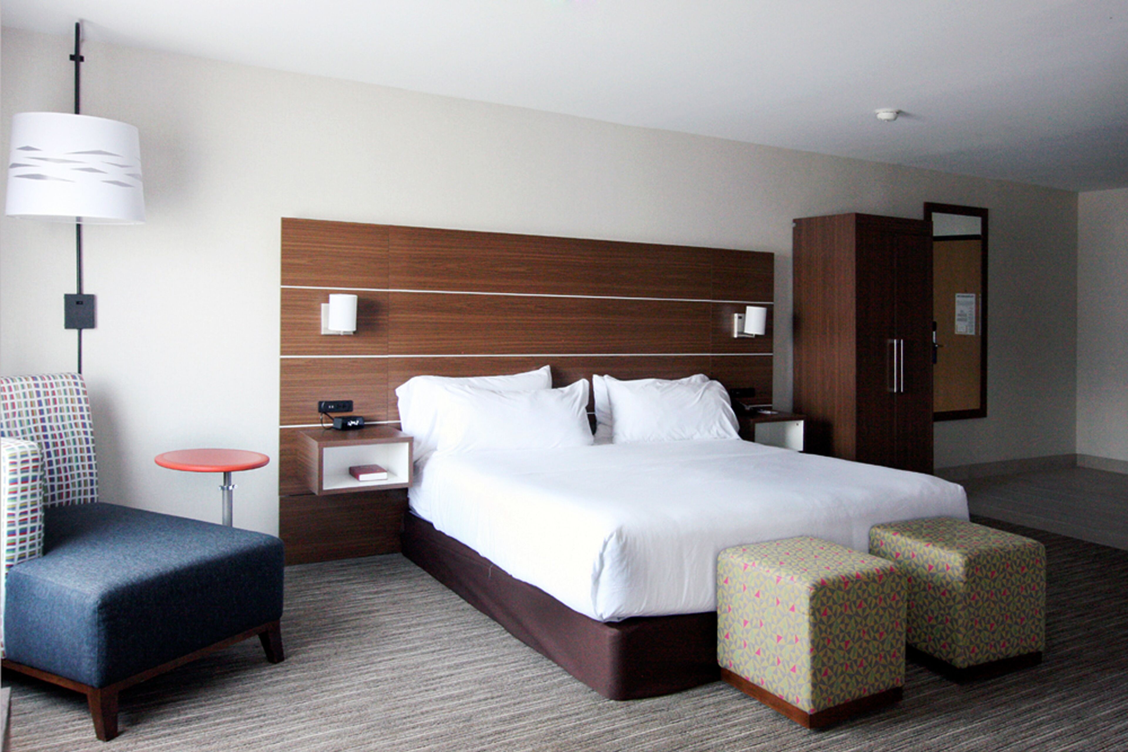 A hotel room with a large bed, a nightstand, a desk, a chair, and a wardrobe.