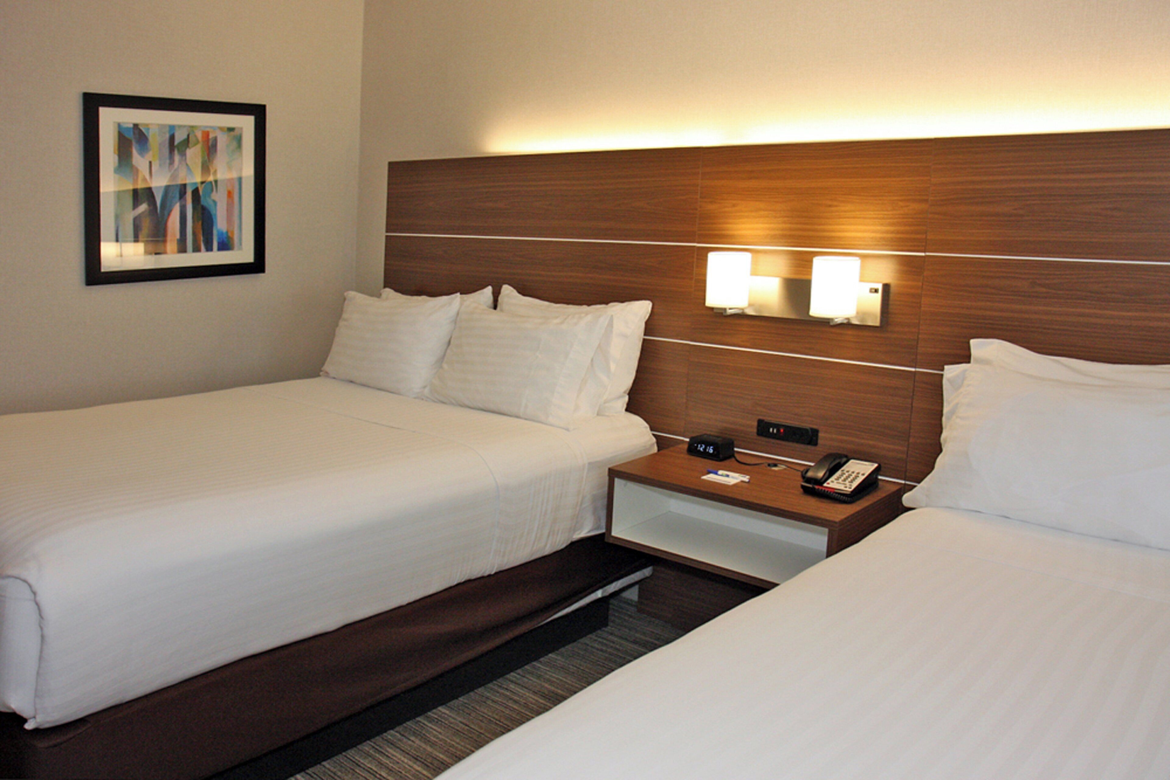 Une chambre d’hôtel avec deux lits, une table de chevet avec un téléphone et un luminaire fixé au mur.