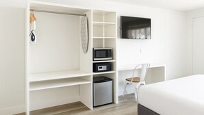 A bedroom with a bed, a TV mounted on the wall, a microwave, a mini fridge, and a chair. - Oneway Brunswick (Brunswick)