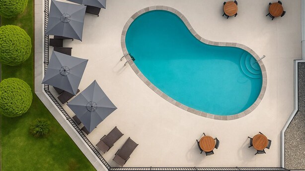 A swimming pool with a curved edge, surrounded by lounge chairs and umbrellas, and a few tables. - Oneway Brunswick (Brunswick)