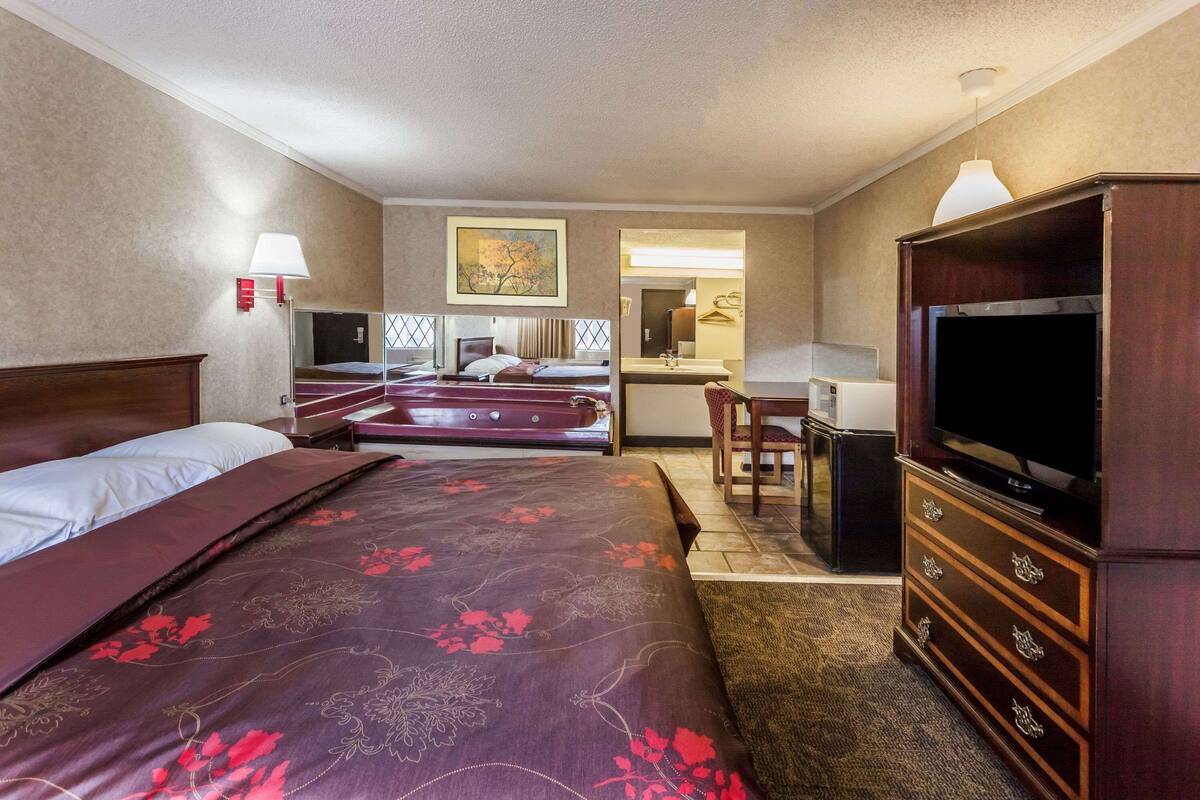A hotel room with a large bed, a desk, a television, and a bathroom visible through an open door.