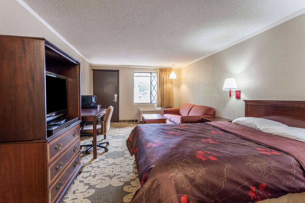 A hotel room with a large bed, a desk with a chair, a television, and a window with curtains.