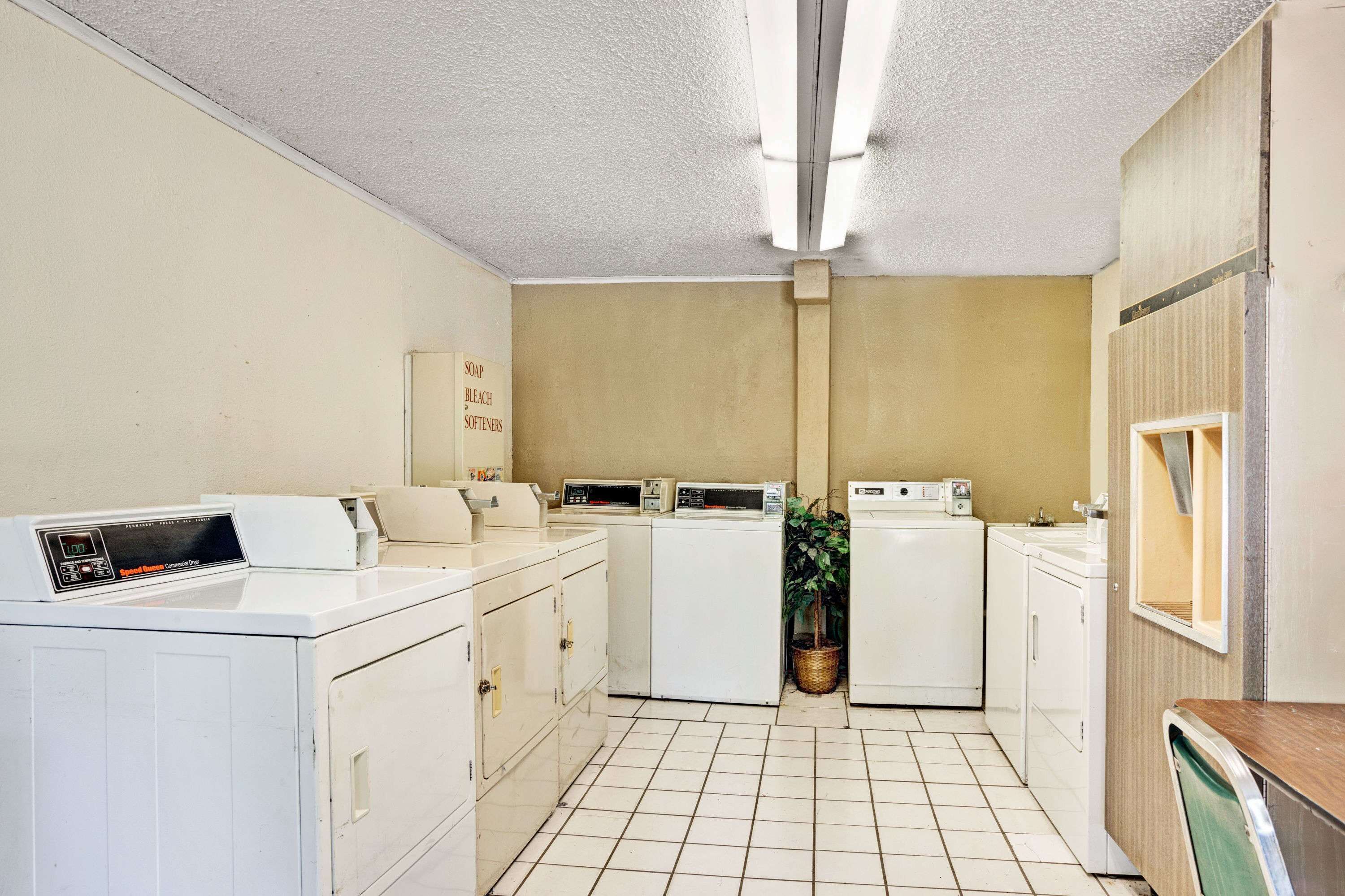 Un lavadero con varias lavadoras, un lavabo y un estante con productos de limpieza.