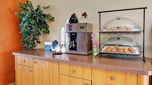 Una estación de café con una máquina de café, una vitrina de pasteles y una planta en maceta.