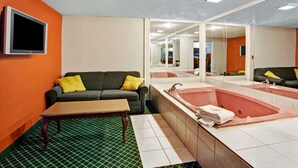 Habitación de hotel con sofá, una mesita, un espejo grande y una bañera.