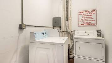 A laundry area with a Whirlpool washer and dryer, a sign indicating operating hours, and a power outlet.