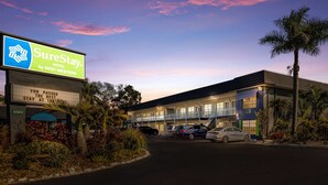 A motel with a sign reading "SureStay by Best Western," featuring a parking lot with several cars, a palm tree, and a clear sky. - SureStay Hotel by Best Western Sarasota Lido Beach (Sarasota)