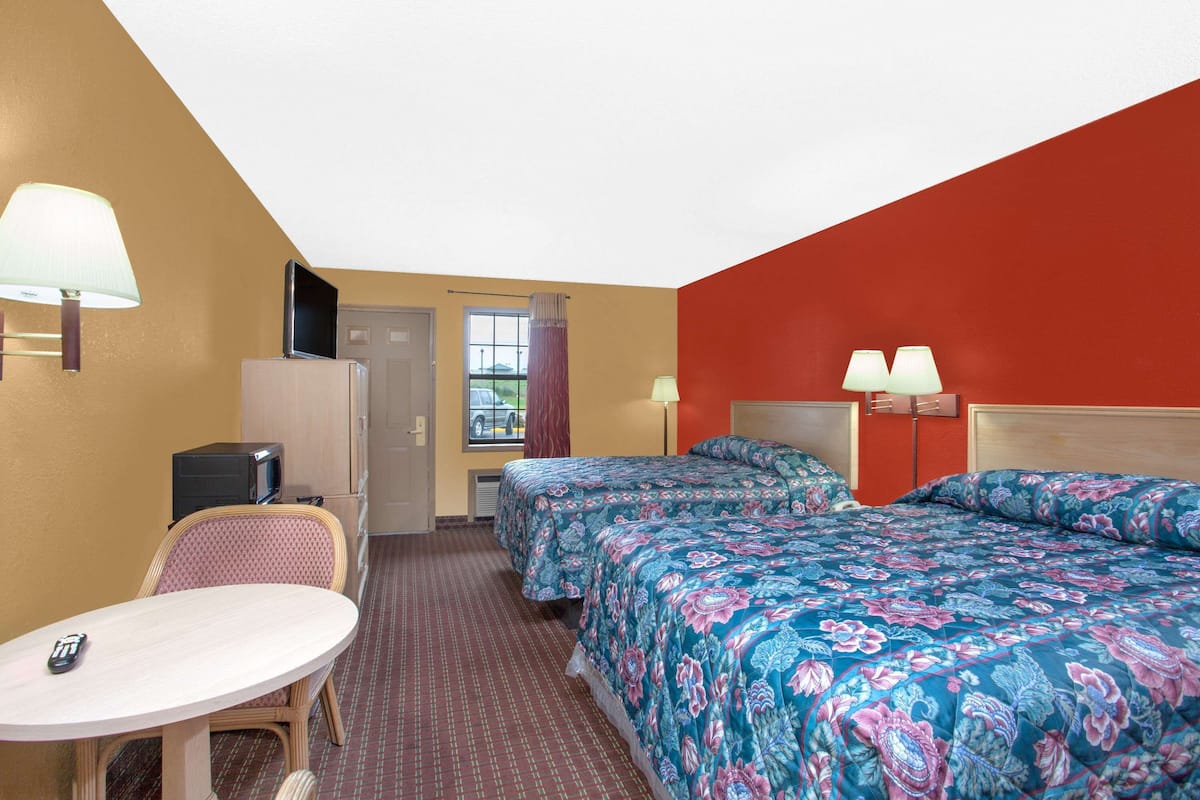 A hotel room with two beds, a desk, a chair, and a television.