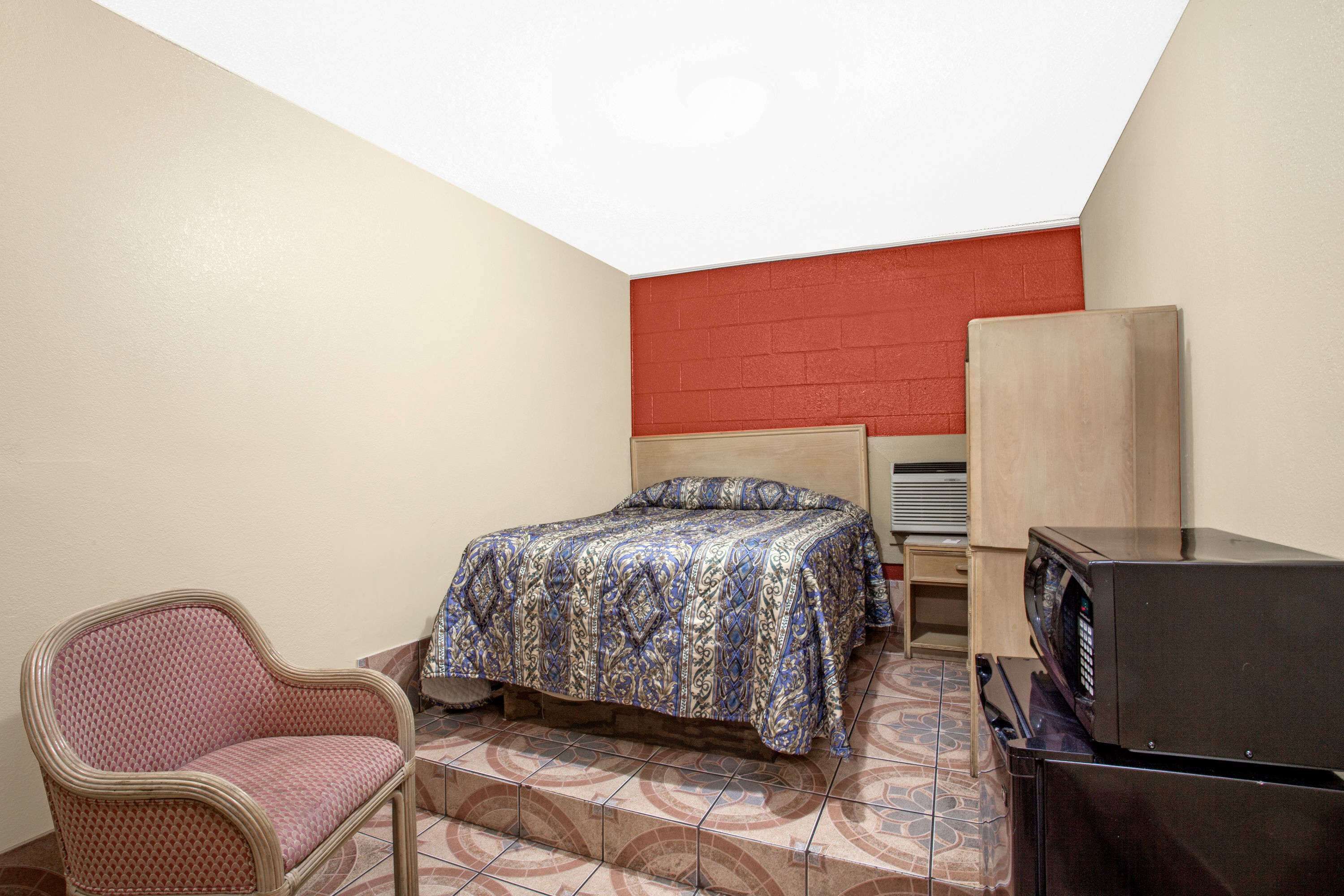 A small, compact room with a bed, a chair, a microwave, and a cabinet.
