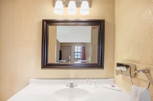 A bathroom with a large mirror, a white sink, and three overhead lights.