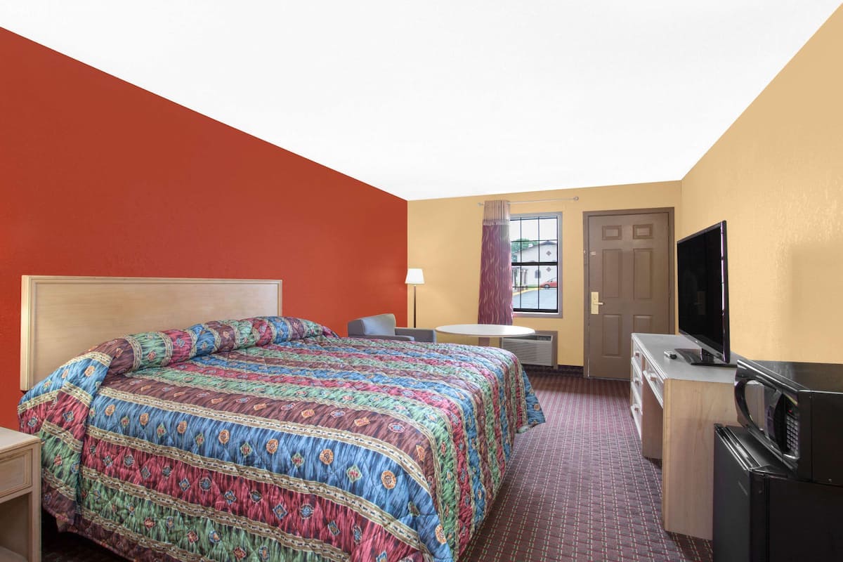 A hotel room with a large bed, a desk, a television, and a microwave.