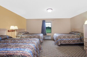 Quarto de hotel com duas camas, uma janela com cortinas, uma luminária no teto e um tapete estampado.