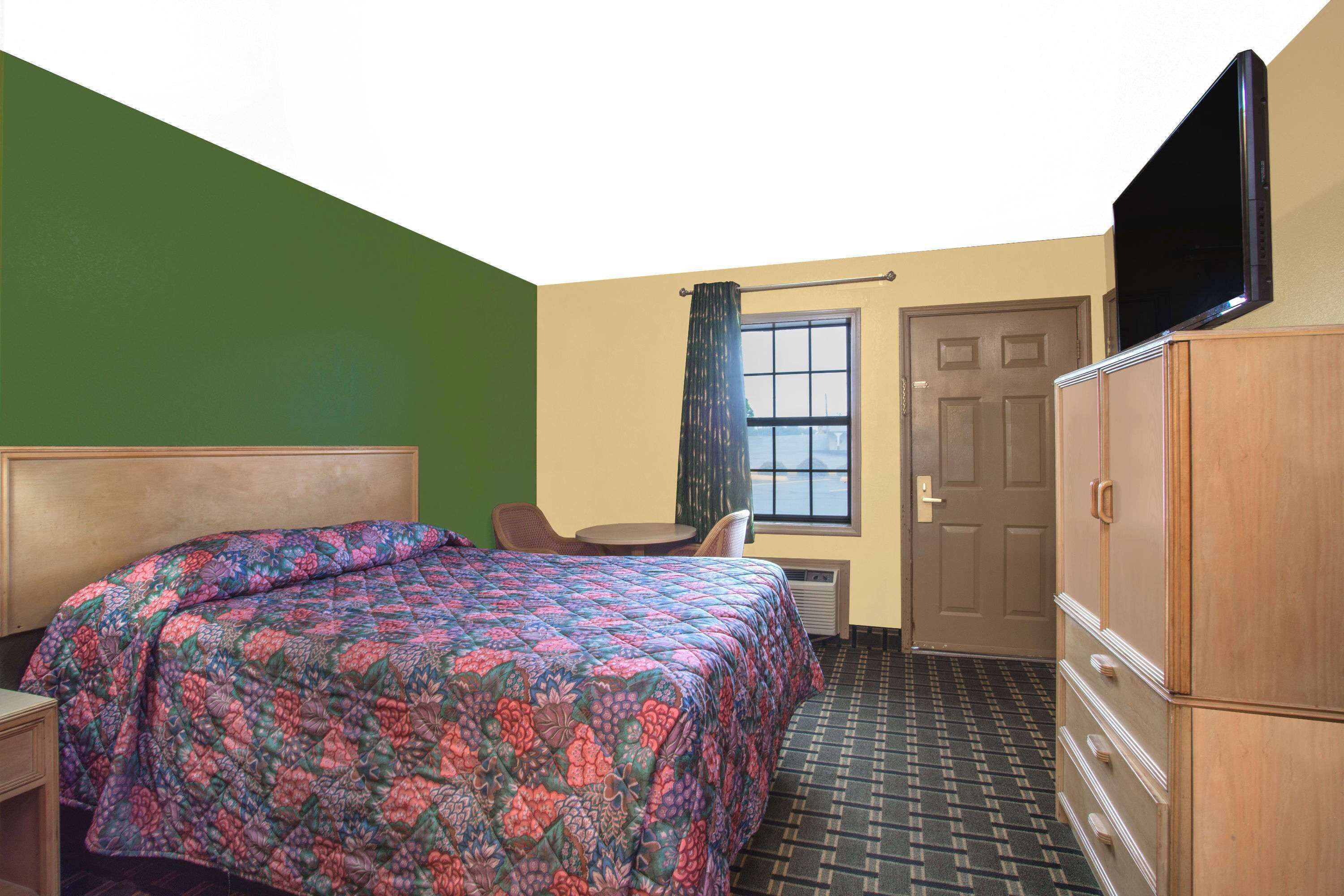 Una habitación de hotel con cama, escritorio, silla, televisor y armario.