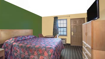 Una habitación de hotel con cama, escritorio, silla, televisor y armario.