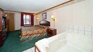 A hotel room with a bed, a nightstand, a lamp, a television, and a bathtub. - Americas Best Value Inn & Suites Warren Detroit (Warren)