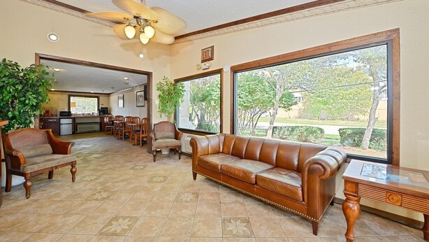 A spacious living area with a leather sofa, wooden chairs, a dining table, and large windows offering a view of the outdoors. - Americas Best Value Inn & Suites Warren Detroit (Warren)