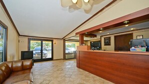A reception area with a wooden reception desk, a leather sofa, and a television. - Americas Best Value Inn & Suites Warren Detroit (Warren)