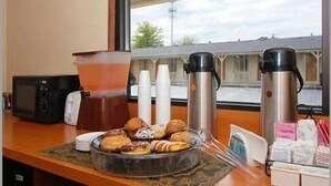 A breakfast setup with pastries and coffee cups, a microwave, and a coffee maker on a counter. - Americas Best Value Inn & Suites Warren Detroit (Warren)