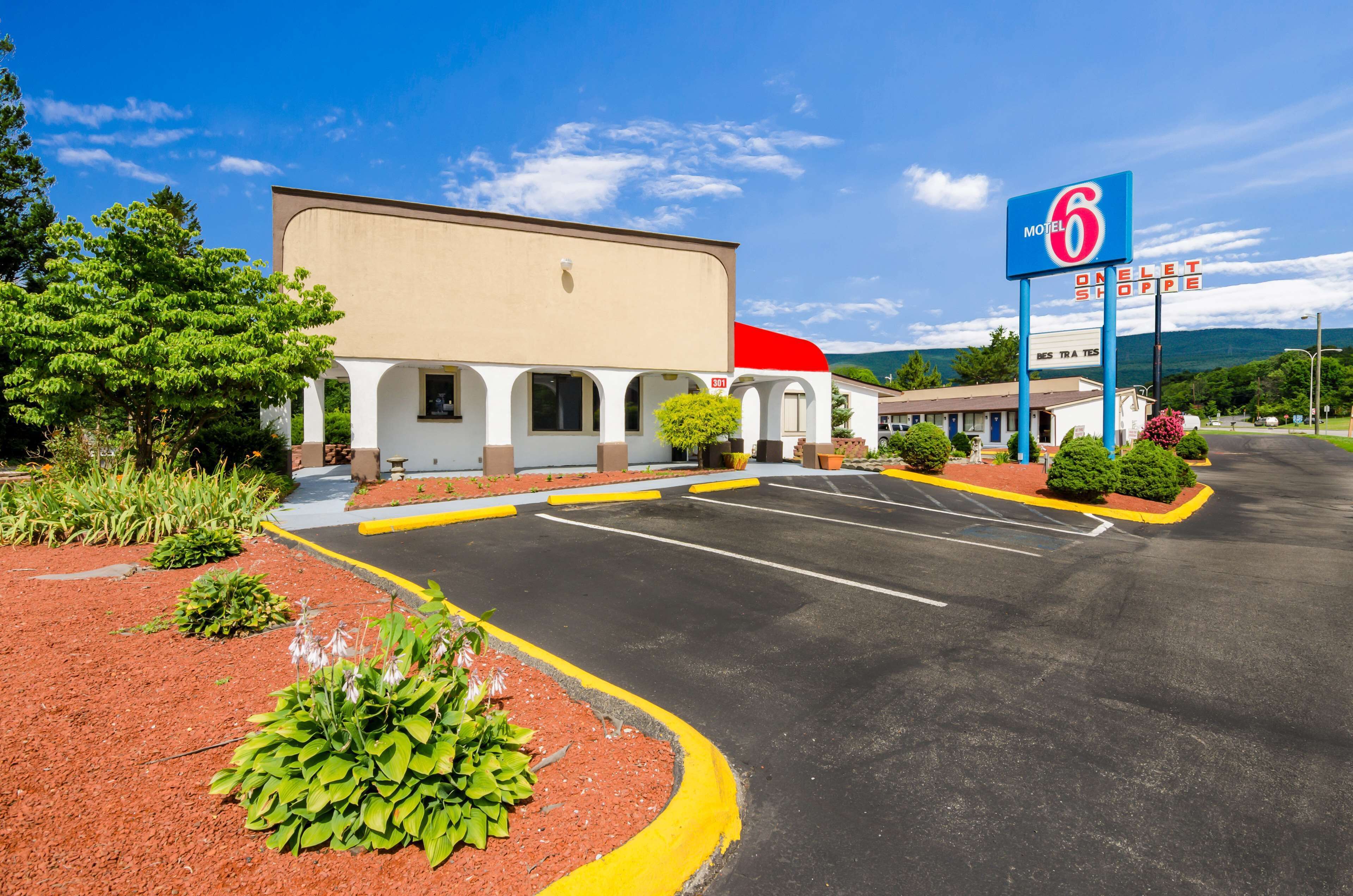 Un motel de la chaîne Motel 6, avec un toit rouge, des murs blancs et un parking bordé de bordures jaunes.