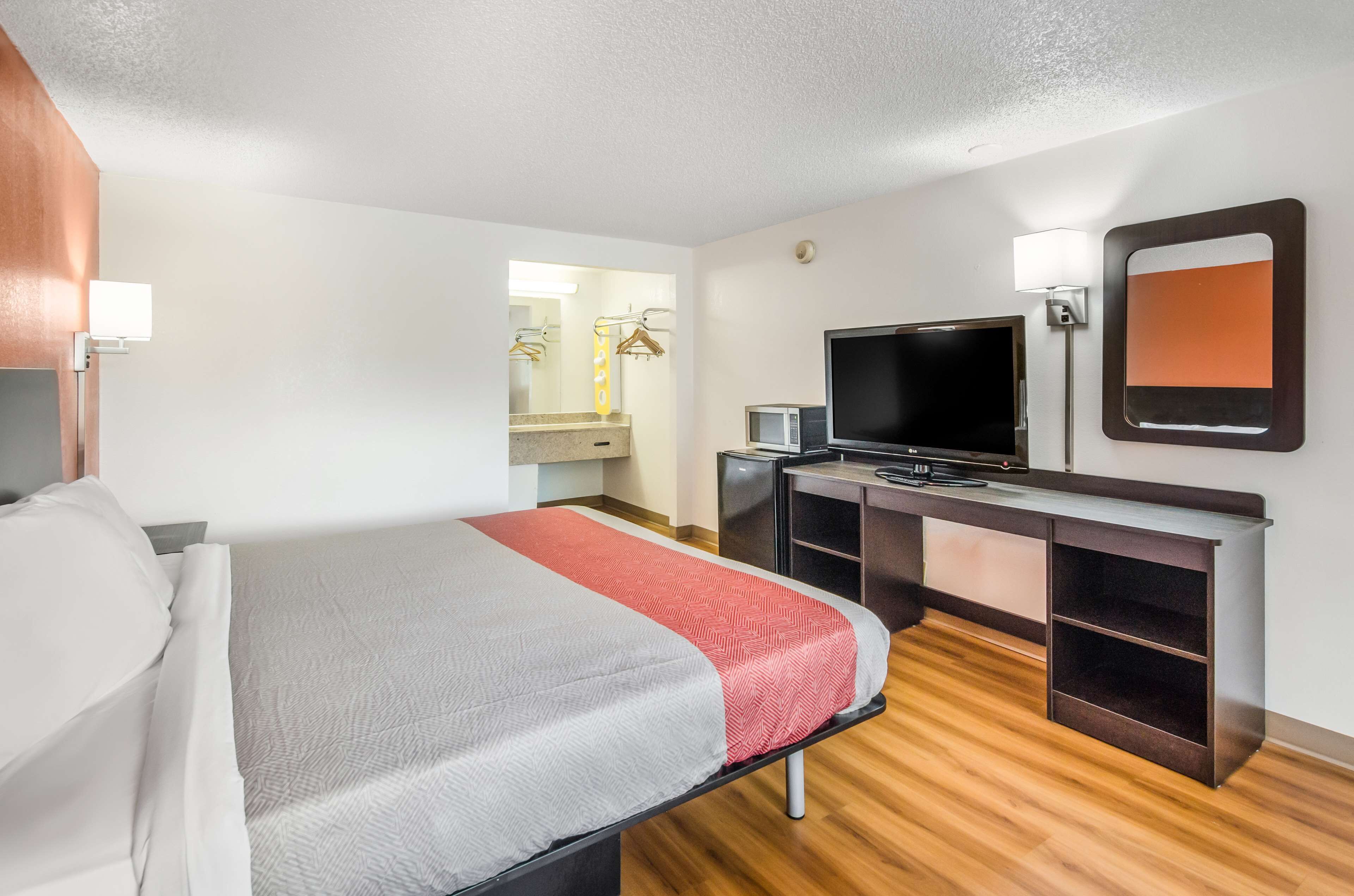 A hotel room with a bed, a desk with a TV, a mirror, and a wardrobe.