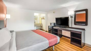 A hotel room with a bed, a desk with a TV, a mirror, and a wardrobe.