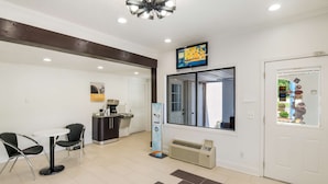 A reception area with a reception desk, two chairs, a coffee station, a digital display, a window, and a door with a poster. - Motel 6 Salem, VA (Salem)