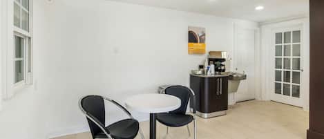 Una cocina compacta con una mesa blanca y dos sillas, una pequeña barra y un refrigerador.