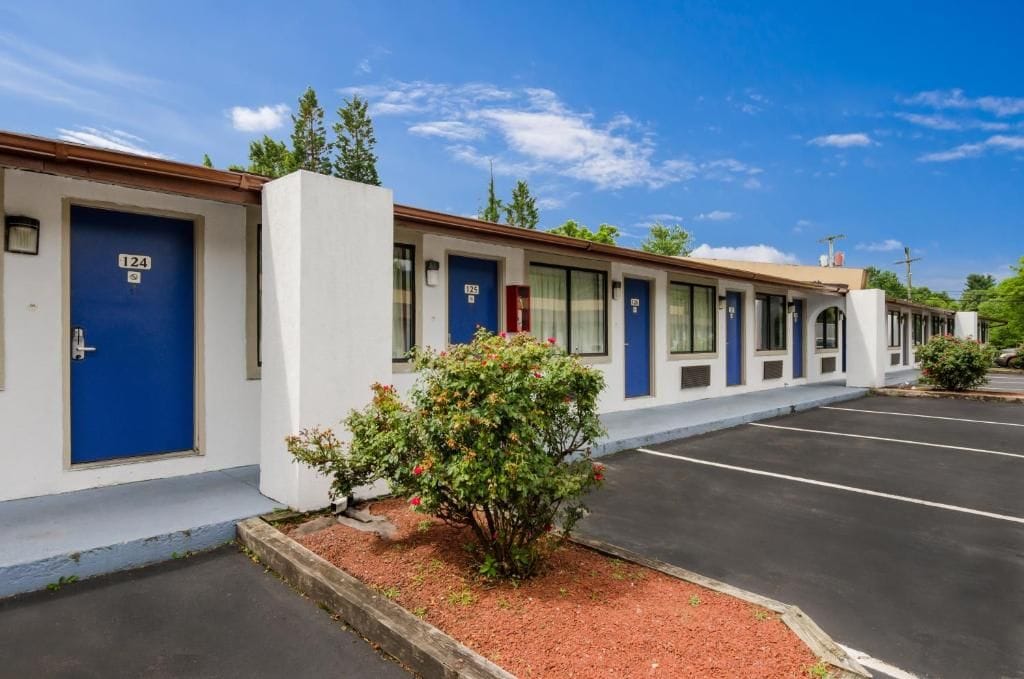 Een rij motelkamers met blauwe deuren, genummerd 124, en een parkeerplaats.