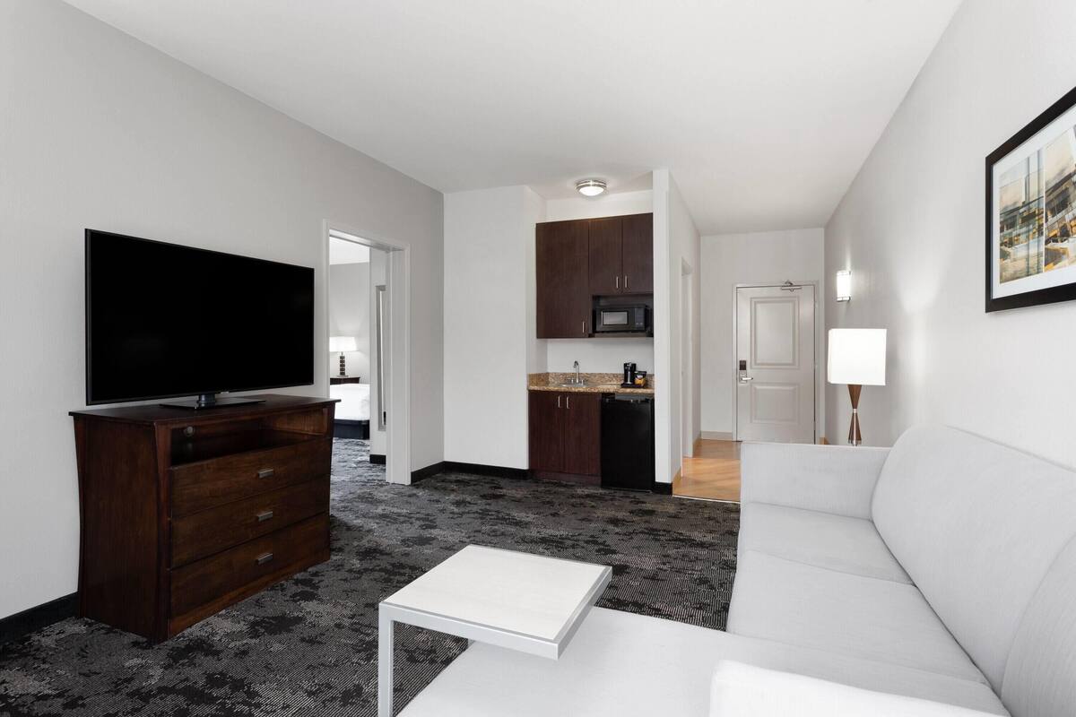 A modern living room with a flat-screen TV, a white coffee table, and a grey sofa.