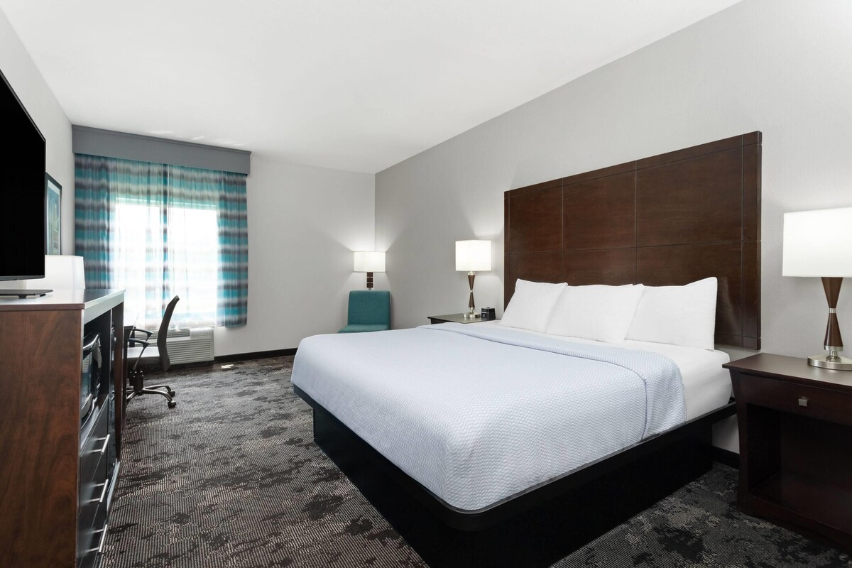 A hotel room with a large bed, two bedside tables with lamps, a desk with a chair, and a television.