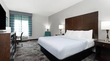 Quarto de hotel com uma cama grande, duas mesas de cabeceira com luminárias, uma escrivaninha com cadeira e uma televisão.