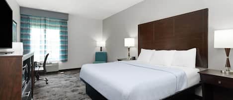 A hotel room with a large bed, two bedside tables with lamps, a desk with a chair, and a television.