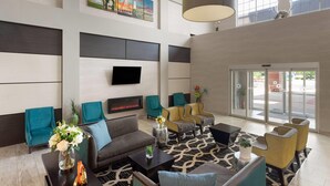 Un vestíbulo amplio con diseño moderno, que incluye un televisor de pantalla plana, asientos cómodos, una chimenea y ventanas grandes con vistas al exterior.
