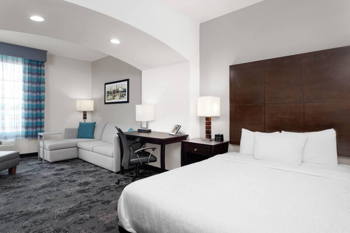 A hotel room with a large bed, a desk with a chair, a sofa, two lamps, and a framed picture on the wall.