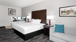 Habitación de hotel con una cama grande, un sofá blanco, un escritorio con lámpara y cuadros en las paredes.