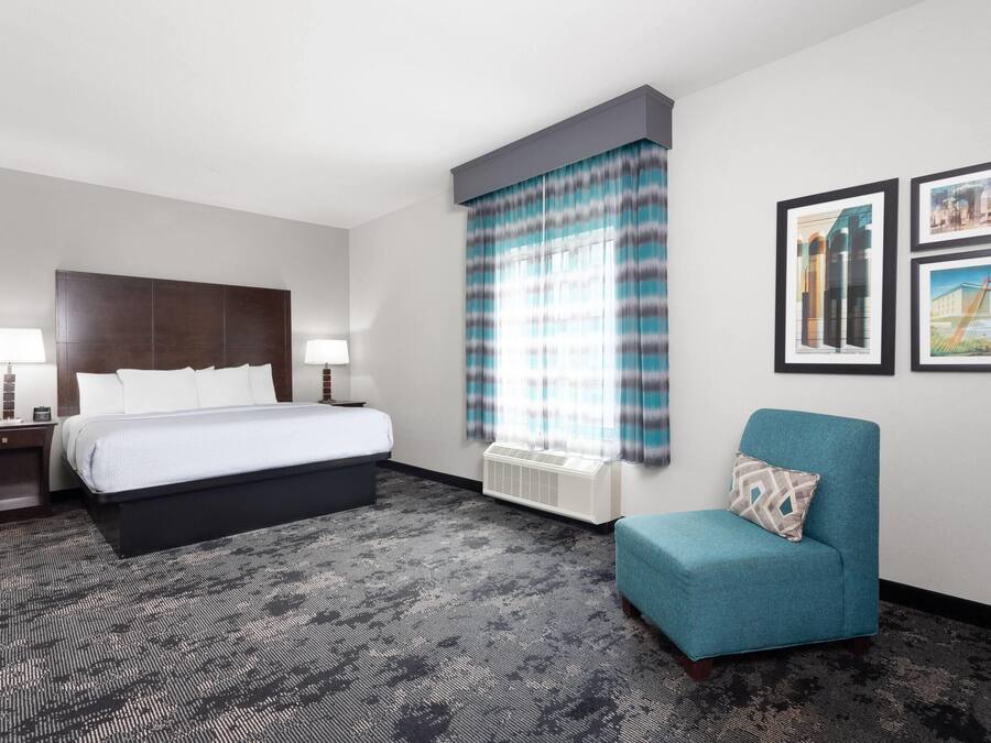 Une chambre d’hôtel avec un lit, des tables de chevet, un radiateur, un fauteuil bleu et des tableaux encadrés accrochés au mur.