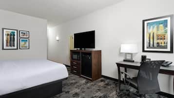 A hotel room with a bed, a desk with a computer, a TV, and framed pictures on the walls.
