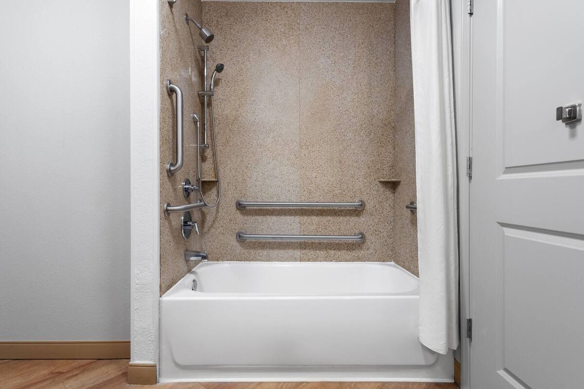 A standard bathroom with a bathtub, grab bars, and a showerhead.