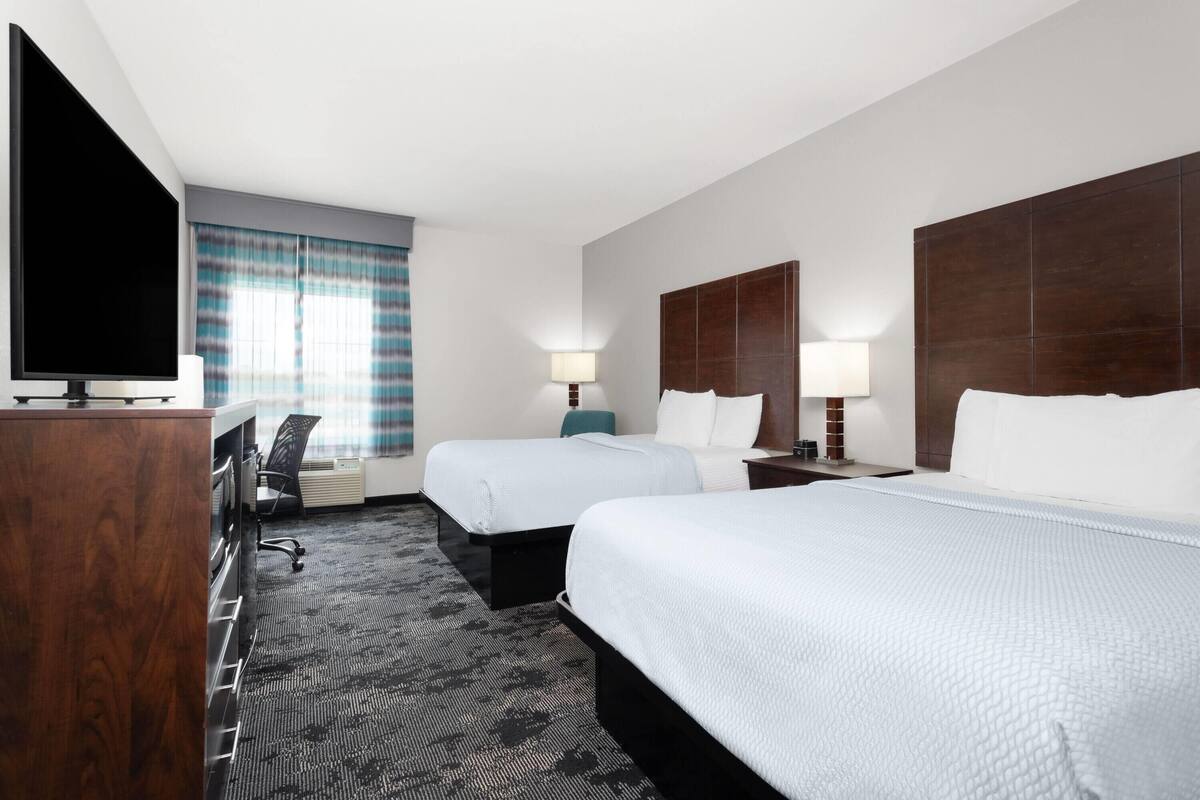 A hotel room with two beds, a TV, a desk, and a chair.