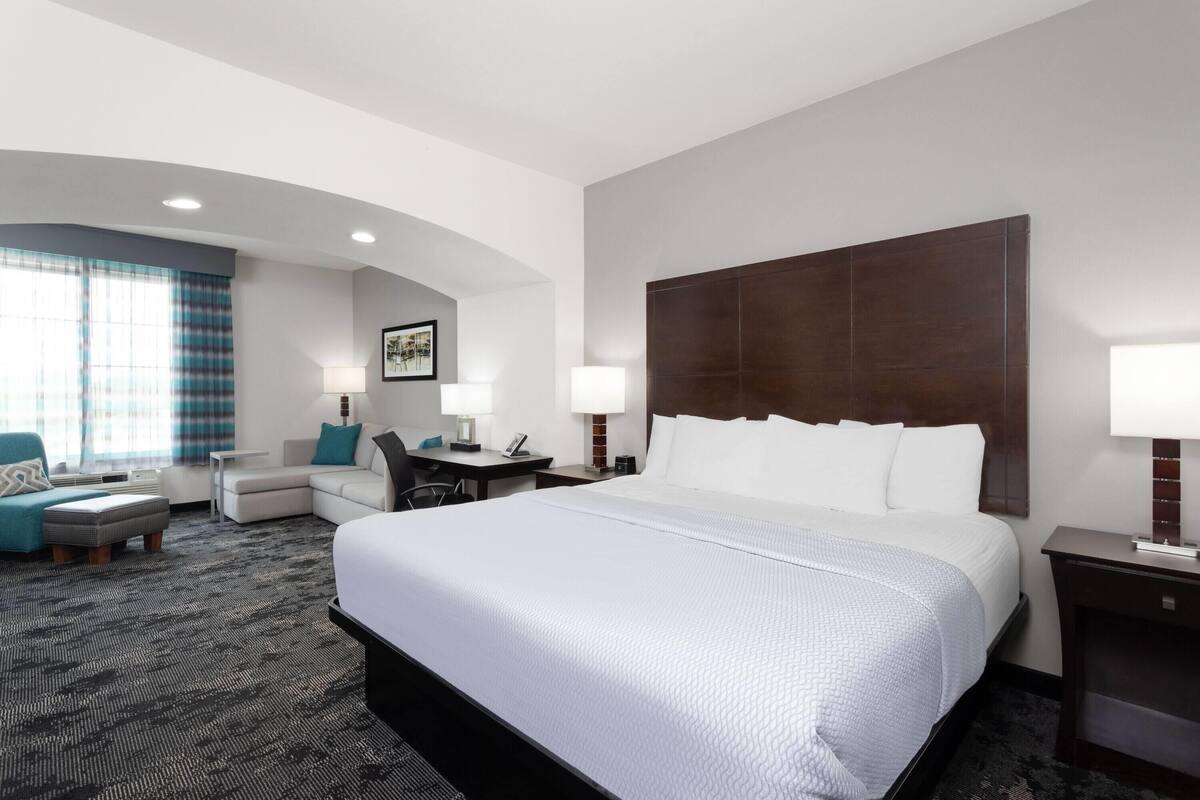 A hotel room with a large bed, a desk, a chair, a sofa, and a lamp.