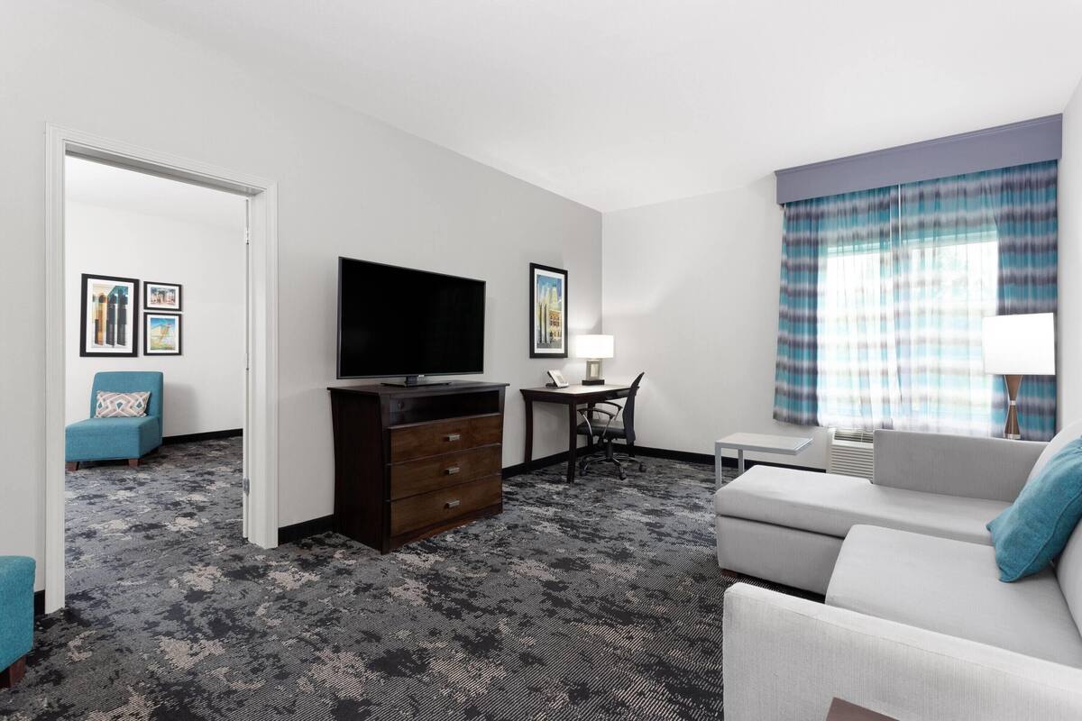 A hotel room with a flat-screen TV, a desk, a sofa, and a chair.