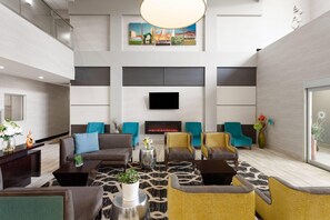 A modern hotel lobby with a fireplace, comfortable seating, a flat-screen TV, and a large window. - La Quinta Inn & Suites by Wyndham Columbus - Edinburgh (Columbus)