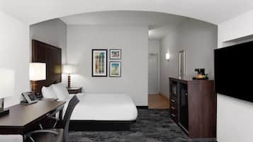 Habitación de hotel con cama, escritorio, silla, lámpara, televisor y una obra de arte en la pared.