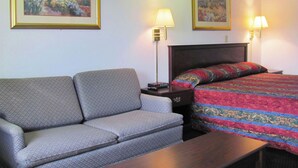 A hotel room with a sofa, a bed with a colorful bedspread, two wall-mounted lamps, and a nightstand with a remote control. - M Star Columbus North (Columbus)