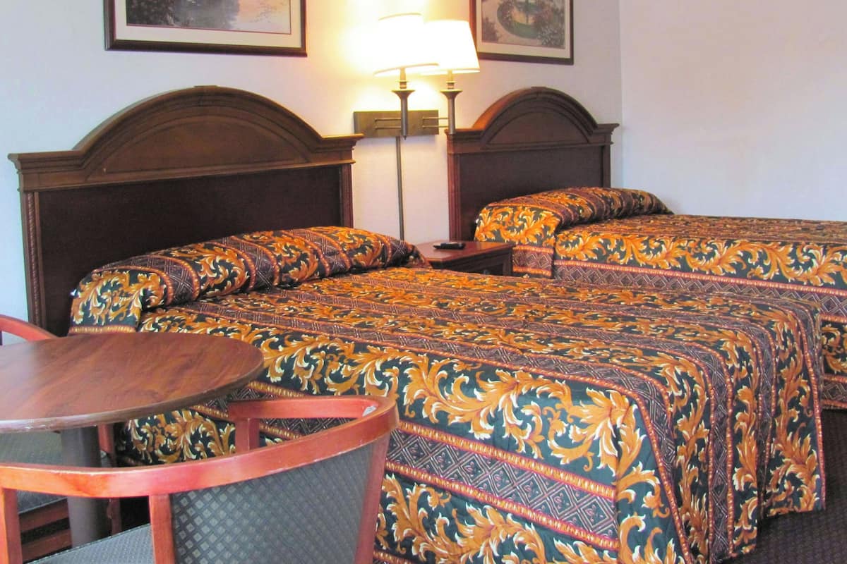 A hotel room with two beds, a small table, and a chair.