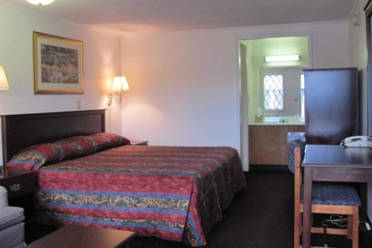 A hotel room with a bed, a desk, a chair, a television, and a bathroom visible through an open door.