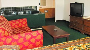 A compact living space with a sofa, a small table, a television, and a kitchenette area. - M Star Columbus North (Columbus)